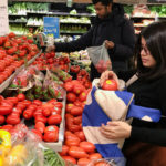 An Indian woman picking a tomato at teh grocery store and putting it into her grocery backpack