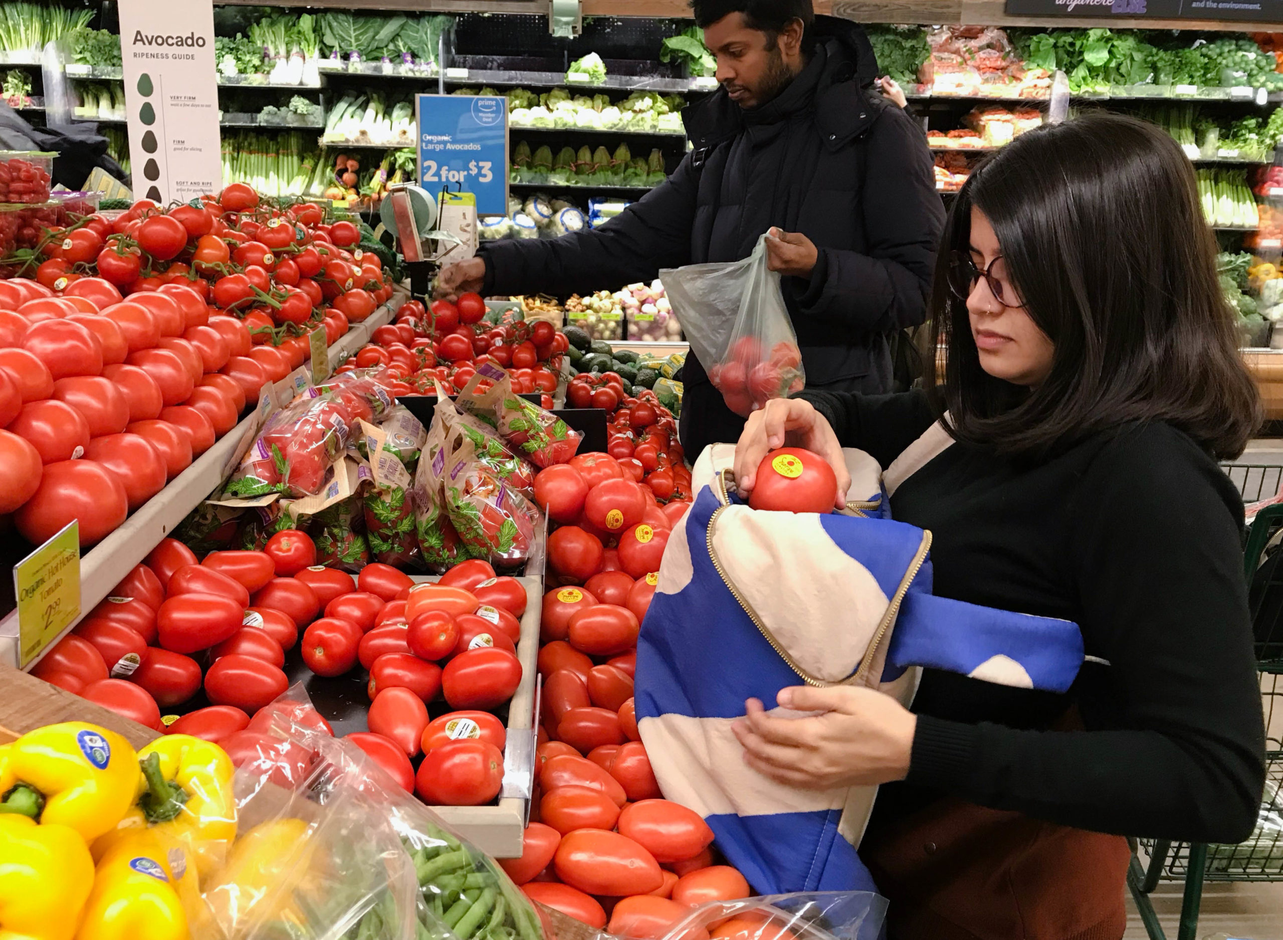 An Indian woman picking a tomato at teh grocery store and putting it into her grocery backpack