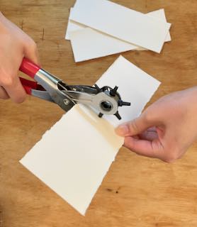 using a leather punch to make a hole in the center of a rectangular piece of watercolor paper
