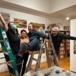 four people hanging off of and between two ladders after hanging prints in a gallery