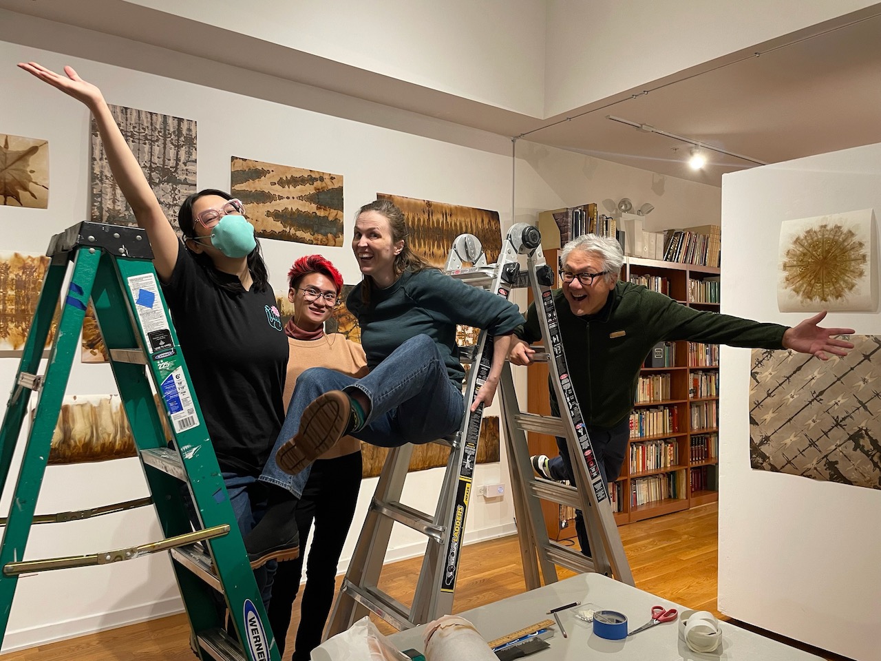 four people hanging off of and between two ladders after hanging prints in a gallery