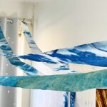 a pulled back view of four, narrow cyanotype banners running across a ceiling. Each is a different shade of blue