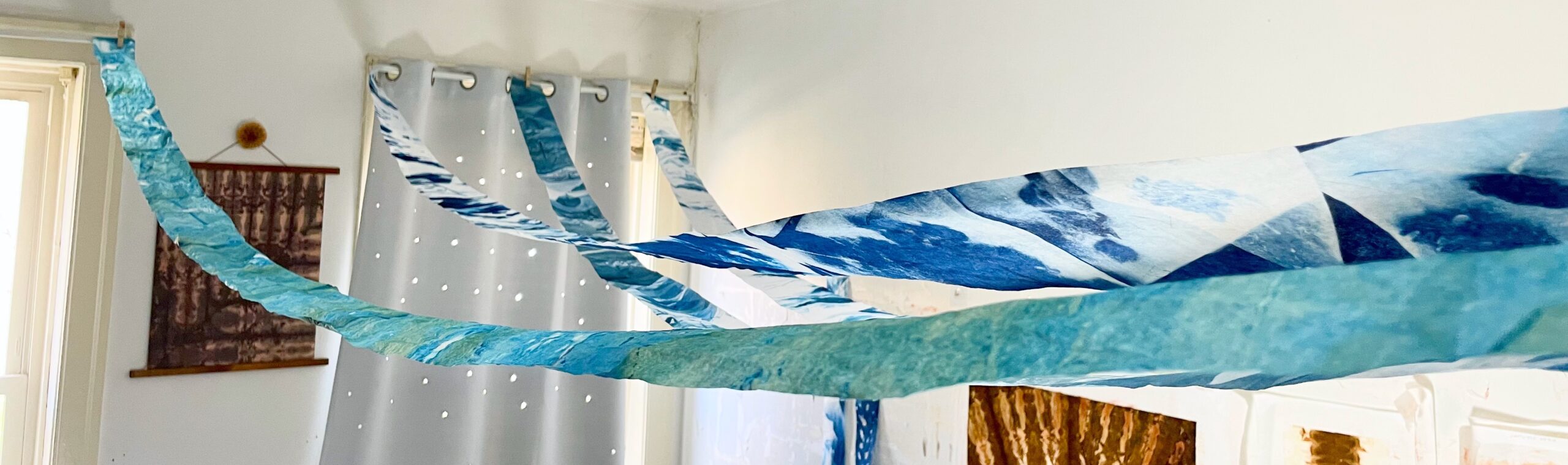 a pulled back view of four, narrow cyanotype banners running across a ceiling. Each is a different shade of blue